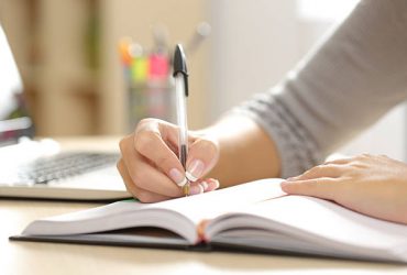 Close up of a woman hand writing in an agenda on a desk at home or office
